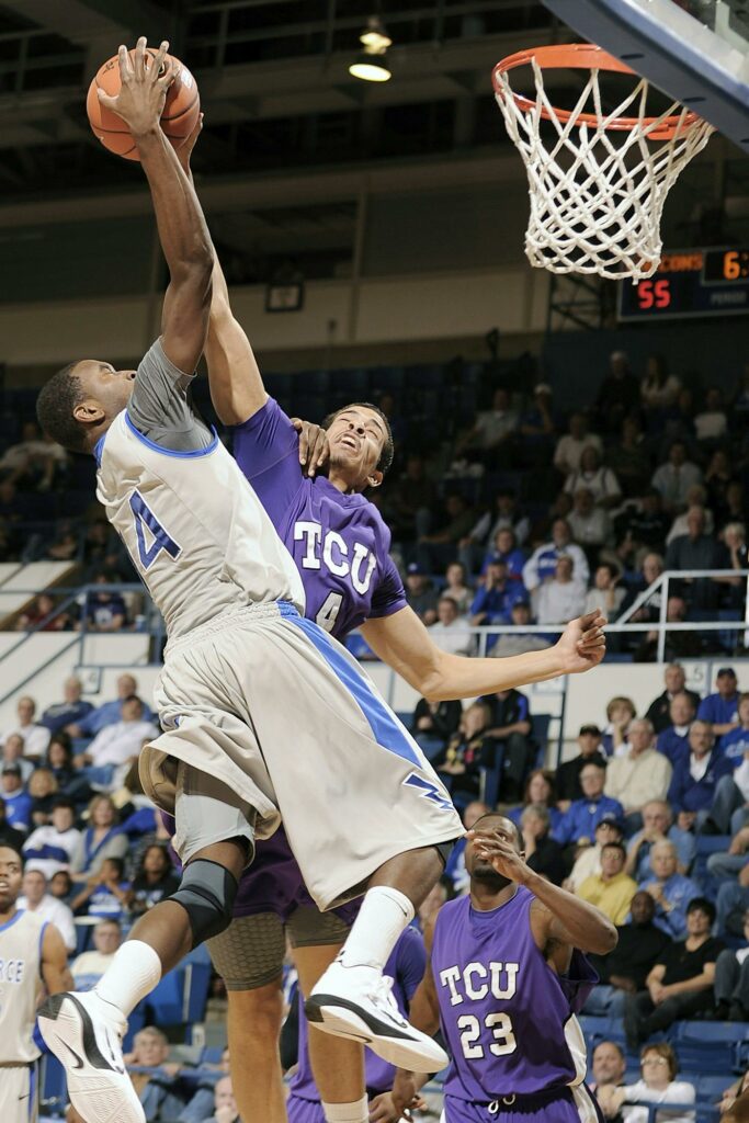 A college basketball player trying to dunk with another defending them.