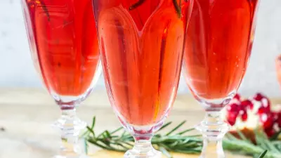 Three pomegranate mimosas in champagne flutes garnished with pomegranates and rosemary