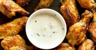 A black plate filled with pickle brined chicken wings with ranch dressing in the middle