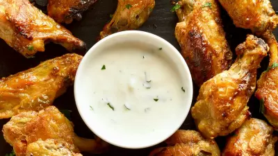 A black plate filled with pickle brined chicken wings with ranch dressing in the middle