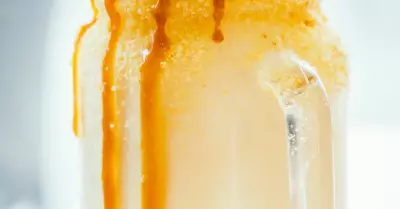 A boozy caramel milk shake in a glass jar with caramel popcorn and a straw