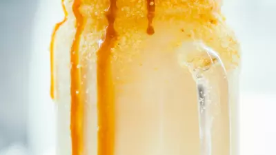 A boozy caramel milk shake in a glass jar with caramel popcorn and a straw