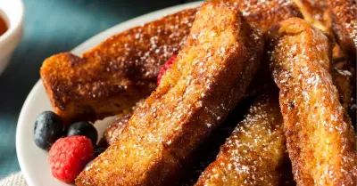 A plate filled with french toast sticks with blueberries and raspberries behind it