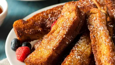 A plate filled with french toast sticks with blueberries and raspberries behind it