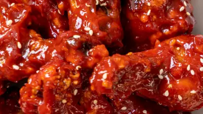 An overhead shot of korean gochujang wings sprinkled with sesame seeds on a white plate.