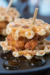 mini chicken and waffles on a black plate with honey butter and a toothpick