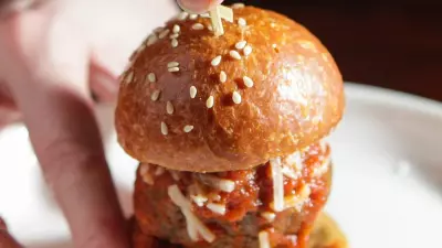 Hands holding a mini meatball slider with sesame seeds on the bun