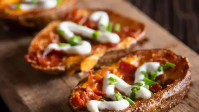 Mini potato skins topped with bacon, green onion and sour cream on a wooden serving board.