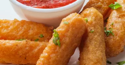 A plate filled with crispy and golden mozzarella sticks with marinara sauce on the side