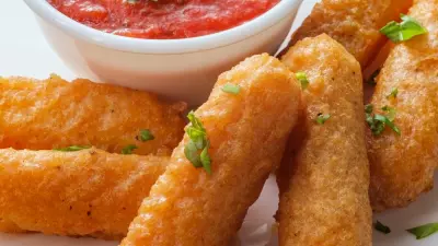 A plate filled with crispy and golden mozzarella sticks with marinara sauce on the side