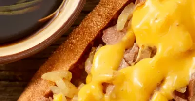 A prime rib sandwich on a toasted bun topped with melted cheese and served with au jus