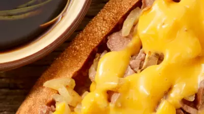 A prime rib sandwich on a toasted bun topped with melted cheese and served with au jus