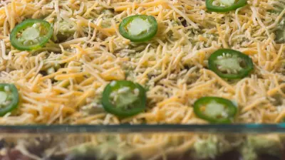 Race day dip in a glass baking dish topped with sliced jalapeno peppers