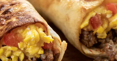 Two toasted sausage breakfast burritos on a wooden cuttingboard.