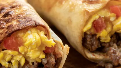 Two toasted sausage breakfast burritos on a wooden cuttingboard.