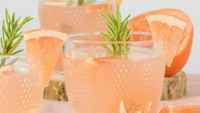 Three plastic cups filled with a grapefruit bourbon rosemary punch with slices of grapefruit and rosemary sprigs in the cups