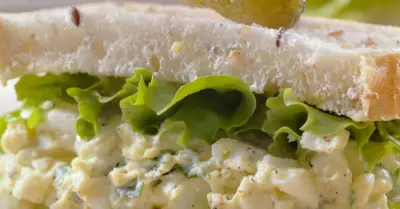 A masters egg salad sandwich on white bread with a pickle on top and lettuce coming out