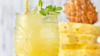 A glass jar filled with pineapple party punch with sliced pineapple in the background