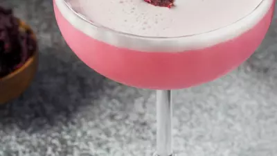A pink habanero hibiscus sour in a coup glass with egg white foam on top