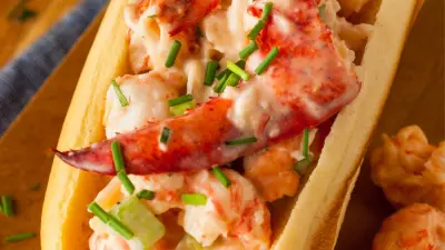 A stuffed lobster roll in between a buttery toasted bun and topped with chives