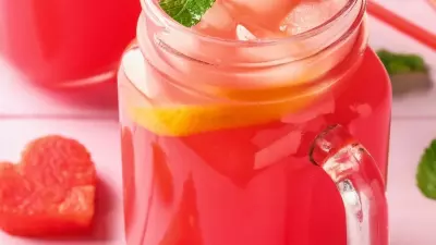 Pink watermelon moonshine in a mason jar with sliced watermelon around it