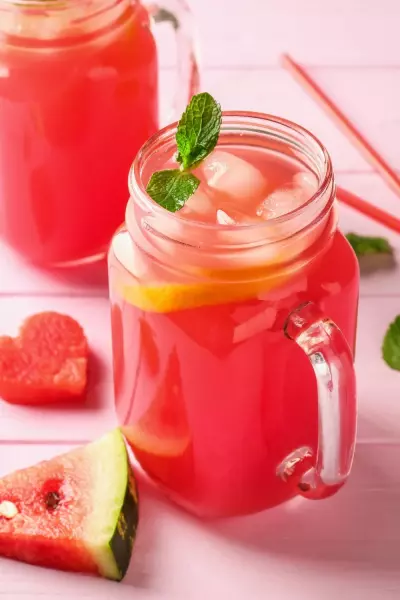 Watermelon Moonshine Recipe 2 Pink watermelon moonshine in a mason jar with sliced watermelon around it
