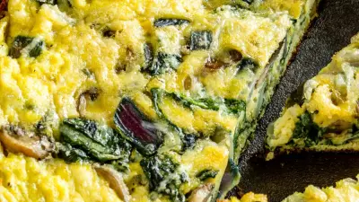 A grilled frittata in a cast iron skillet with spinach showing.