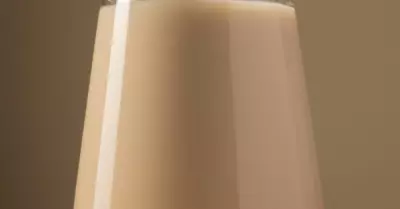 Boozy white hot chocolate in a glass with a straw.