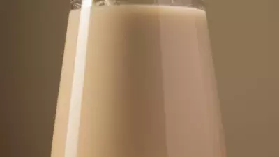 Boozy white hot chocolate in a glass with a straw.