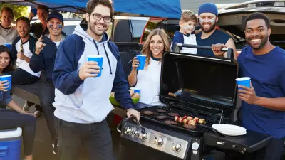 Friends around a grill smiling at a football tailgate party.