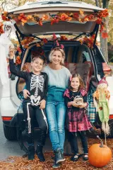A mother and her son and daughter sitting in a car decorated for a trunk or treat halloween tailgate.