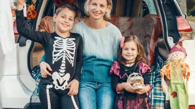 A mother and her son and daughter sitting in a car decorated for a trunk or treat halloween tailgate.