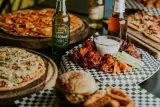 A spread of pizzas, wings, burgers and beer for a super bowl party.