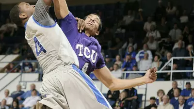 A college basketball player trying to dunk with another defending them.